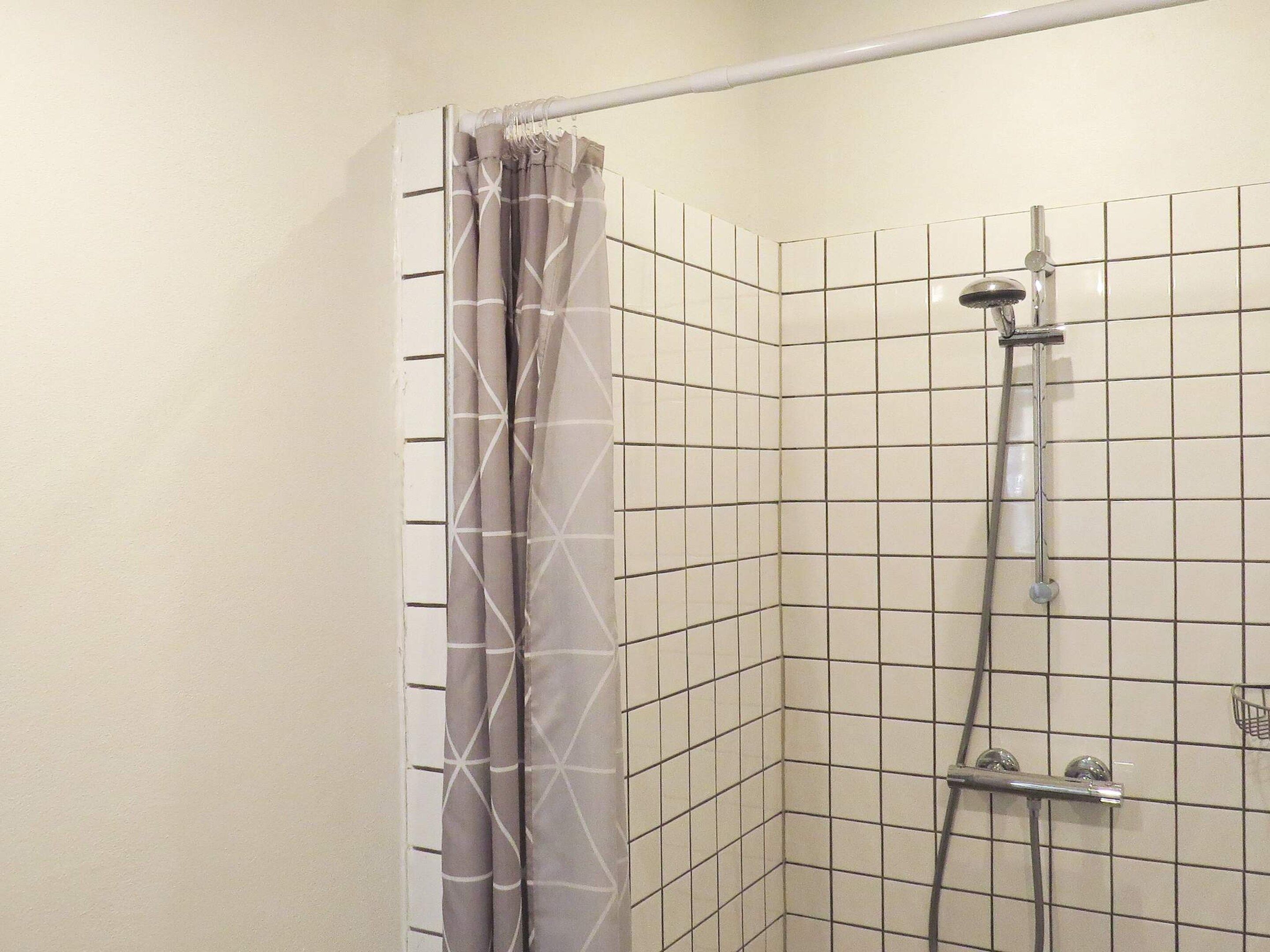 A shower area with a showerhead, curtain, and tiled walls.