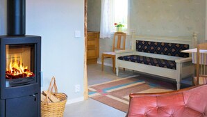 A cozy room with a wood-burning stove, a bench, a chair, and a window with curtains. - 4 Star Holiday Home in Sandhem (Sandhem)