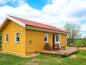 A yellow wooden house with a red-tiled roof, a covered patio with wooden furniture, and a grassy yard. - 4 Star Holiday Home in Sandhem (Sandhem)