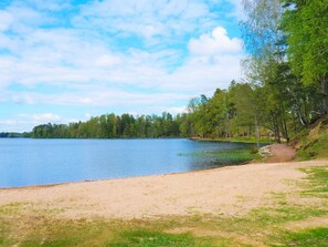 A lakeside view with a sandy beach, trees, and a clear sky. - 4 Star Holiday Home in Sandhem (Sandhem)