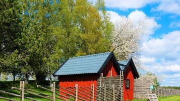 A red wooden structure with a sloped roof, surrounded by a wooden fence and lush green grass.