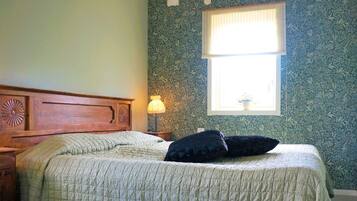 A bedroom with a bed, a nightstand, a lamp, a window, and a floral wallpaper.