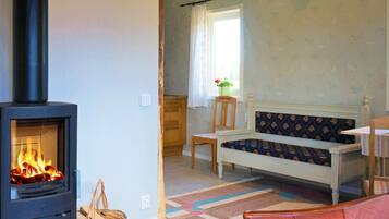 Quarto aconchegante com lareira a lenha, um banco, uma cadeira e uma janela com cortinas.