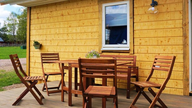 A wooden deck with a table and chairs, a window with a curtain, and a wall-mounted light fixture. - 4 Star Holiday Home in Sandhem (Sandhem)