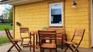 A wooden deck with a table and chairs, a window with a curtain, and a wall-mounted light fixture. - 4 Star Holiday Home in Sandhem (Sandhem)