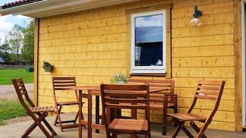 A wooden deck with a table and chairs, a window with a curtain, and a wall-mounted light fixture.