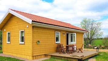 A yellow wooden house with a red-tiled roof, a covered patio with outdoor furniture, and a grassy yard.