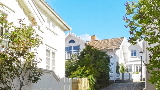 A cobblestone street lined with white buildings, a wooden fence, and trees. - 9 Person Holiday Home in Fiskebackskil (Fiskebackskil)