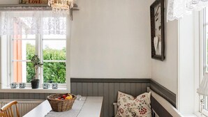 A cozy dining area with a wooden table, a bench with floral cushions, and a window with lace curtains. - 8 Person Holiday Home in Kopingsvik (Kopingsvik)
