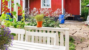 A red wooden house with a porch, a white bench, and various potted plants. - 8 Person Holiday Home in Kopingsvik (Kopingsvik)