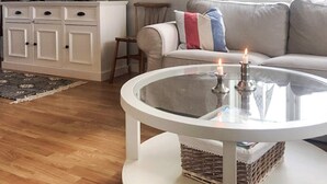 A living room with a glass coffee table, a white cabinet, a sofa with striped pillows, and a television on top of the cabinet. - 8 Person Holiday Home in Kopingsvik (Kopingsvik)