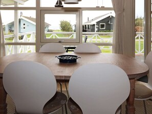 A round dining table with four chairs, a black pan in the center, and a view of houses through a large window.