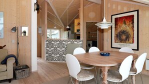 A dining area with a round wooden table and white chairs, a kitchen in the background, and a framed picture on the wall.