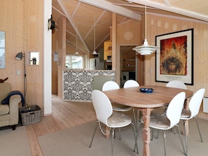 A dining area with a round wooden table and white chairs, a kitchen in the background, and a framed picture on the wall. - 4 Star Holiday Home in Hadsund (Hadsund)