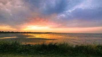 Un paisaje costero con atardecer, un primer plano con hierba y mar tranquilo.