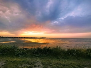 A coastal landscape with a sunset, grassy foreground, and a calm sea.