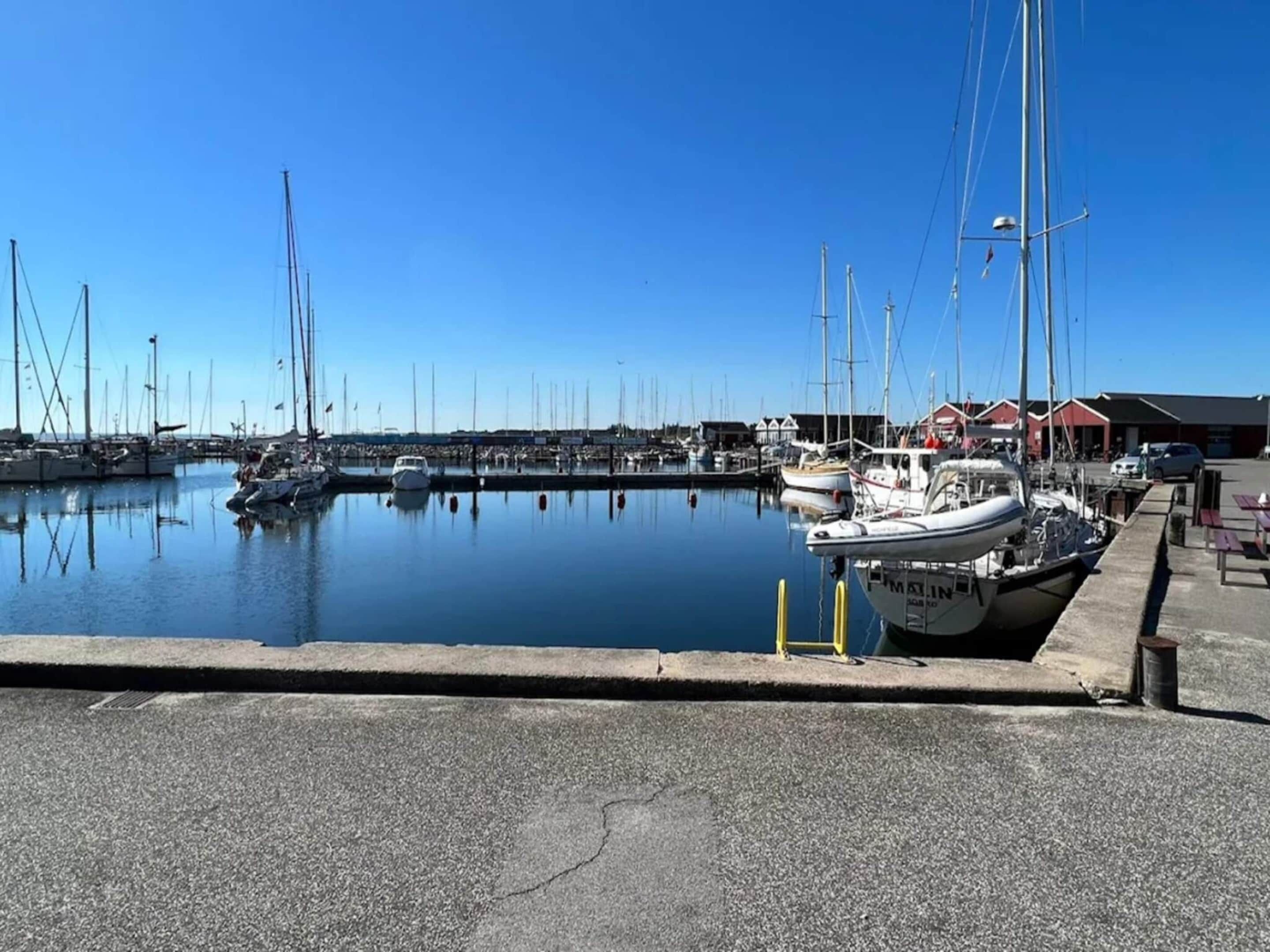 A marina with boats docked, a clear sky, and a building with a red roof in the background.