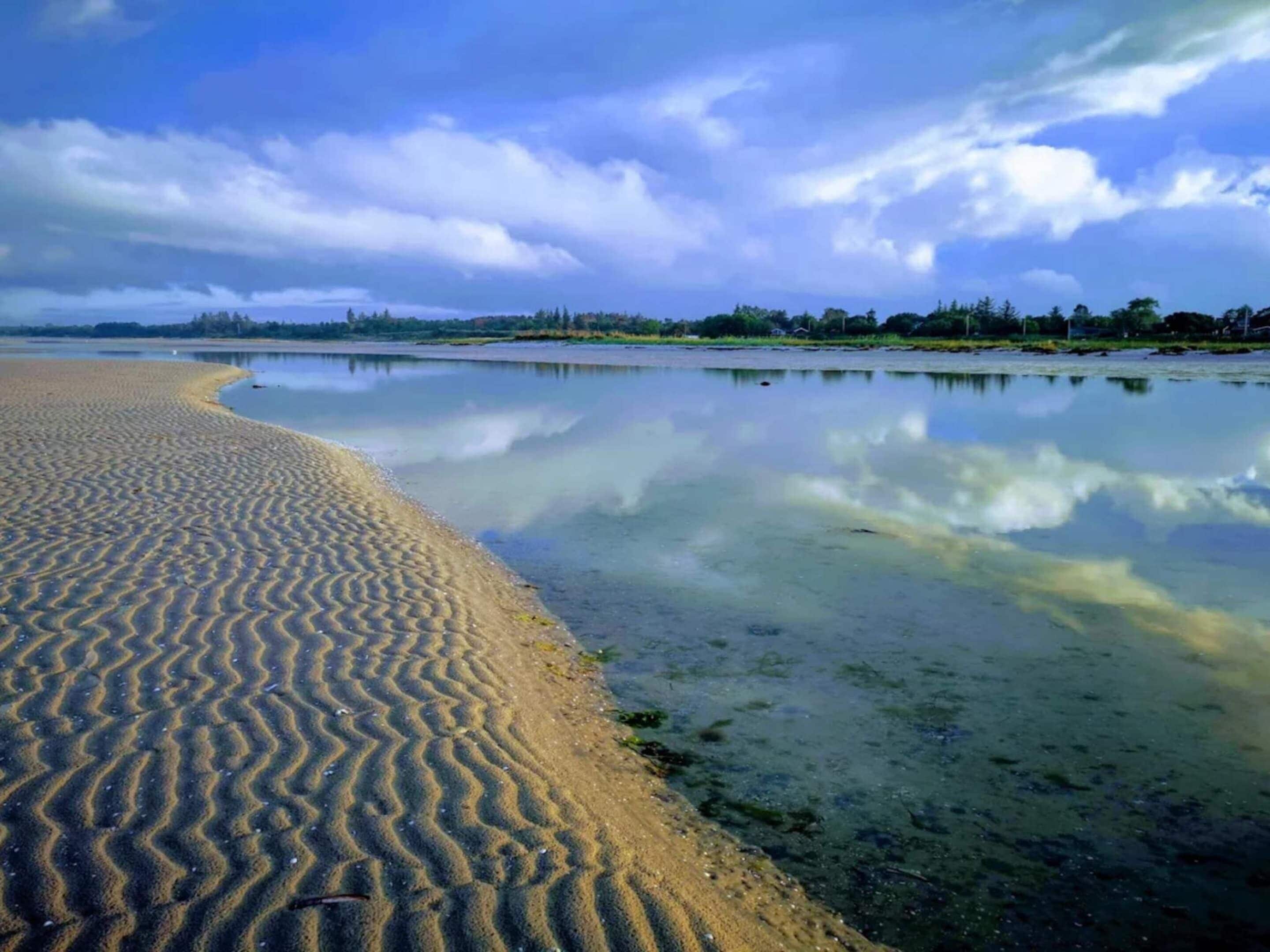 A beach with a sandy shoreline and calm water reflecting the sky.