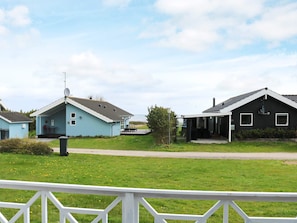 A residential area with two houses, one blue and one black, with a grassy lawn and a white fence in the foreground.