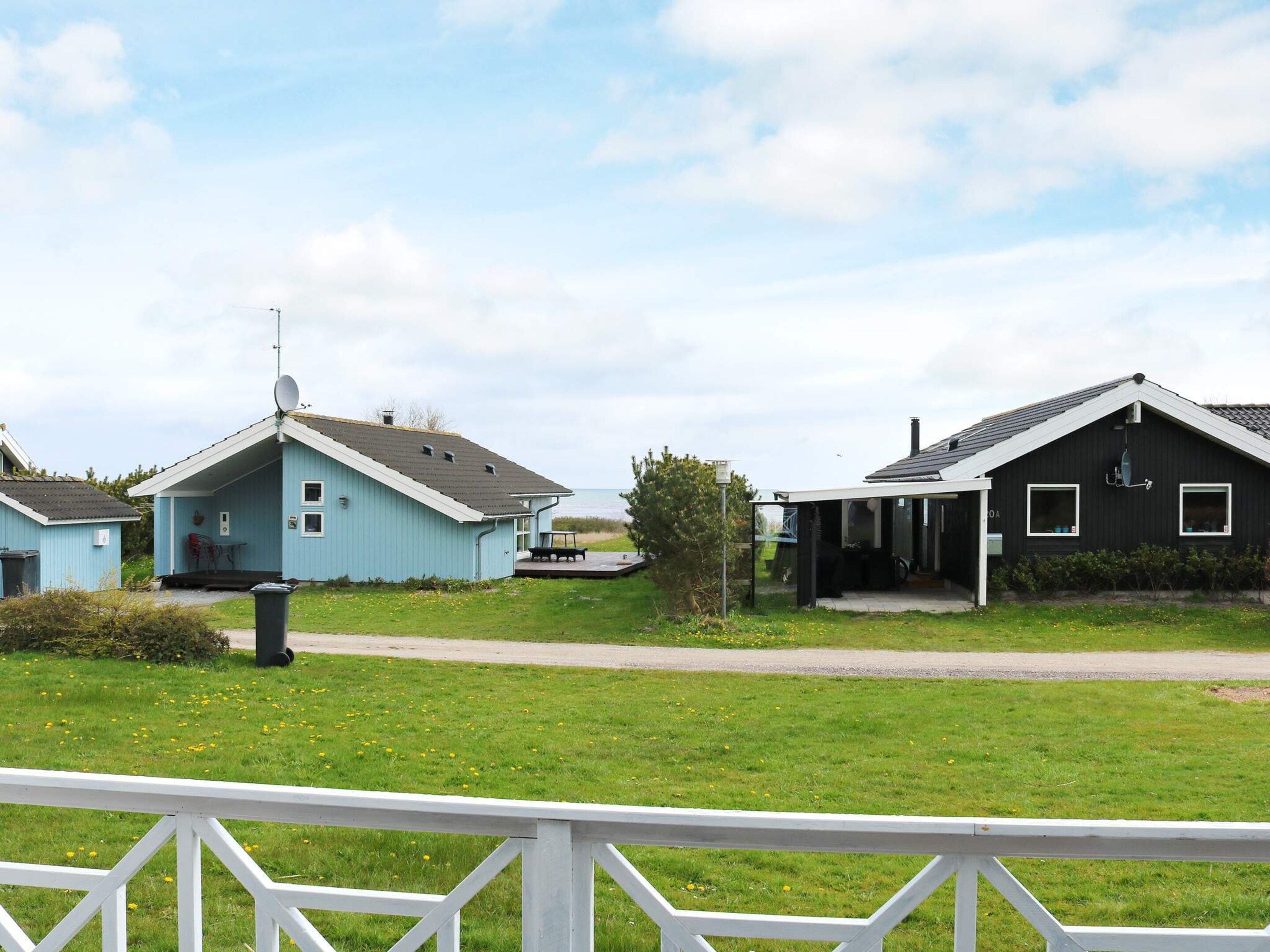 Een woonwijk met twee huizen, een blauw en een zwart, met een gazon en een witte hek in de voorgrond.