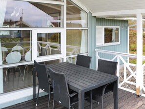 A covered outdoor area with a table and chairs, large windows, and a light blue building. - 4 Star Holiday Home in Hadsund (Hadsund)
