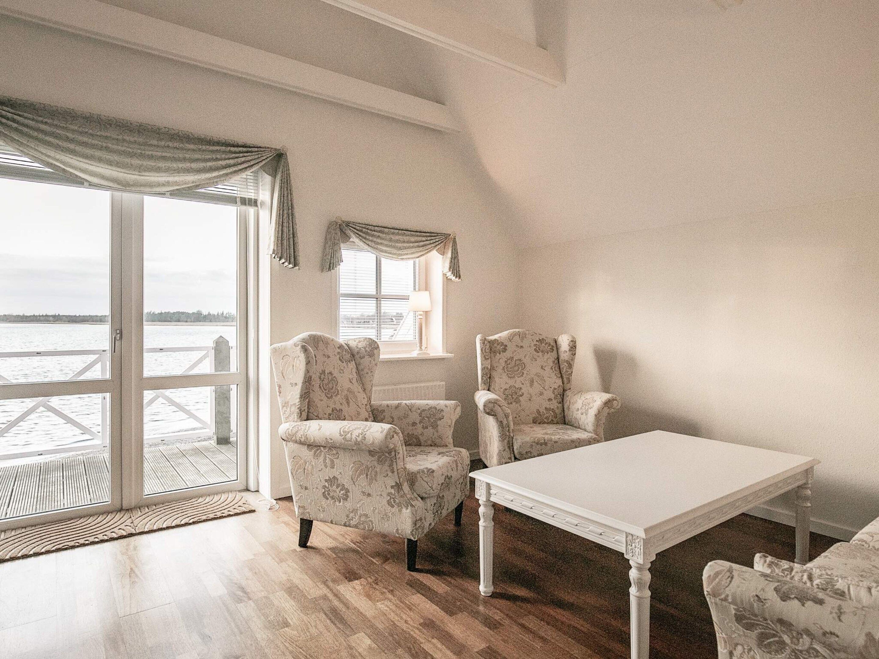 Una habitación con vista al agua, una mesa blanca y dos sillones estampados.