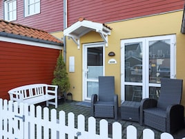 Un patio con muebles de mimbre, una cerca blanca de piquetes y un edificio amarillo con tejado rojo.