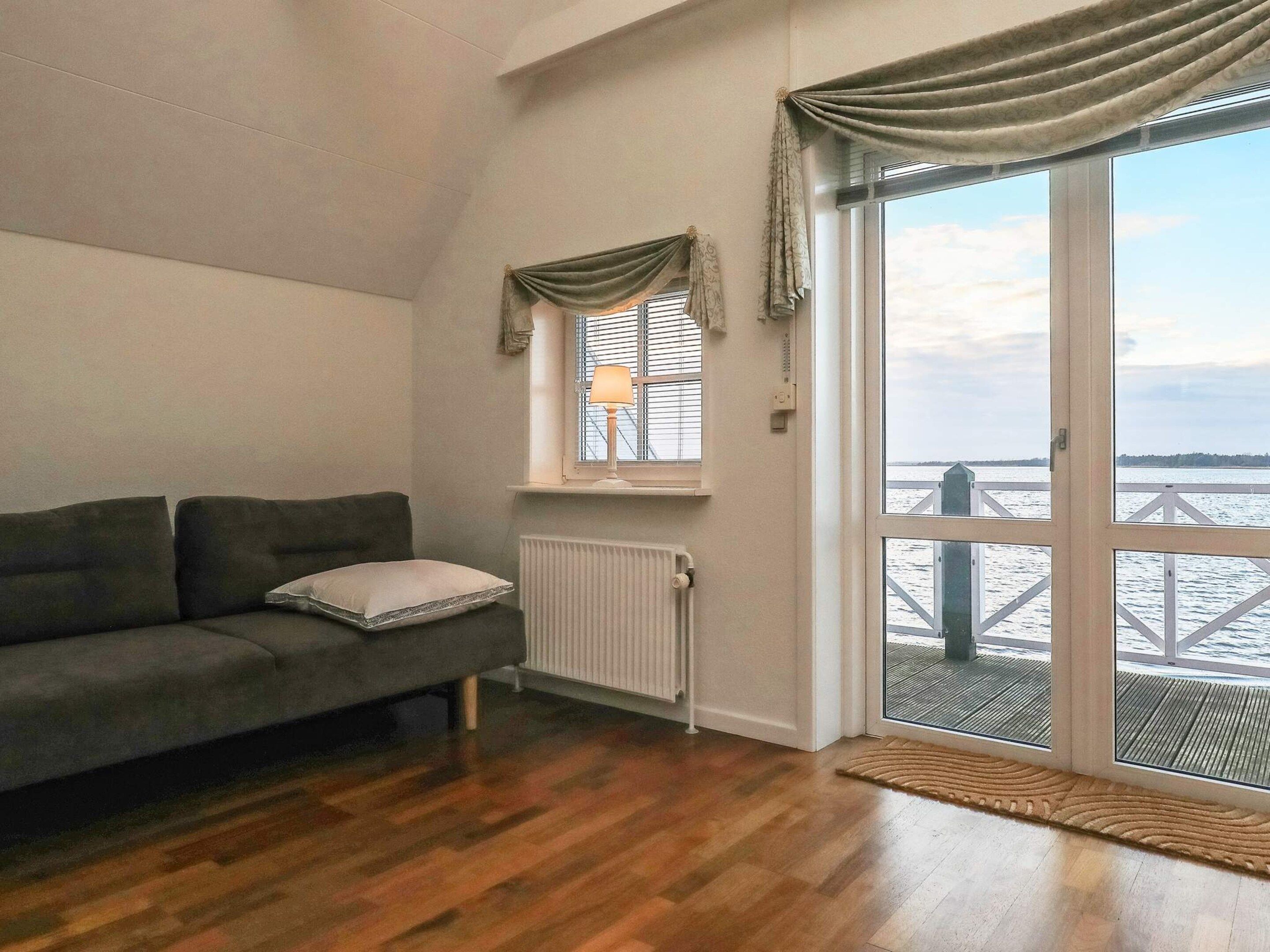 Un salón con sofá, una ventana con cortinas, un radiador y vistas a un muelle.