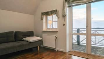 Un salón con sofá, una ventana con cortinas, un radiador y vistas a un muelle.