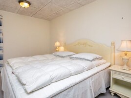 A neatly made bed with a white duvet and pillows, a bedside table with a lamp, and a ceiling light fixture.
