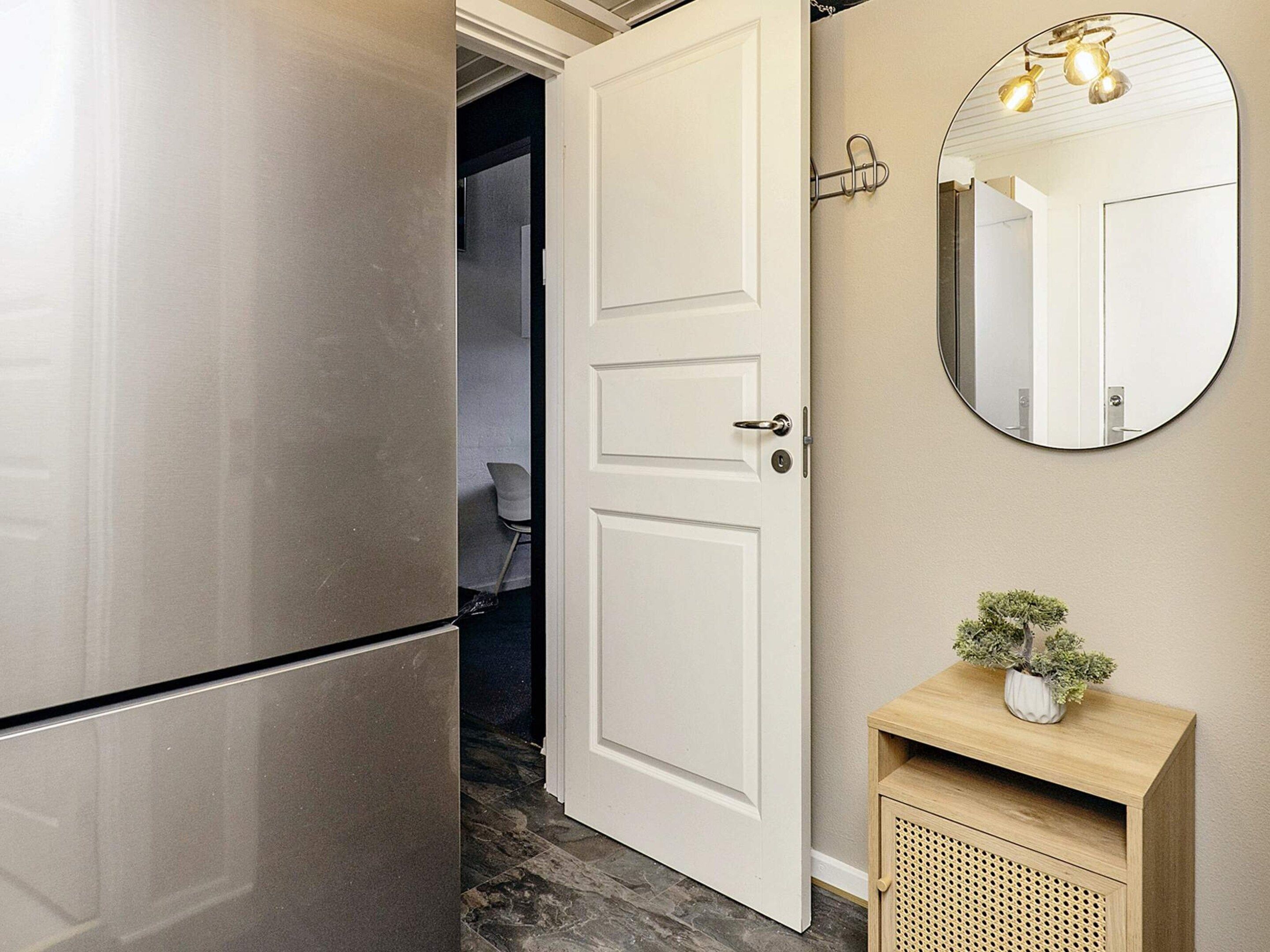 Una cocina moderna con un refrigerador de acero inoxidable, una puerta blanca y un espejo redondo con luces arriba.