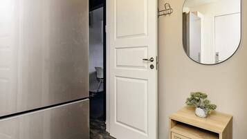 Una cocina moderna con un refrigerador de acero inoxidable, una puerta blanca y un espejo redondo con luces arriba.