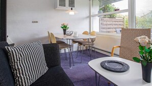 A modern living room with a sofa, a dining table, and chairs. There is a window with blinds, a ceiling light, and a wall-mounted cabinet. - 4 Star Holiday Home in Vaeggerlose (Vaeggerlose)
