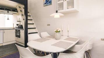 Una cocina moderna con armarios blancos, una estufa negra y una mesa de comedor blanca con cuatro sillas.