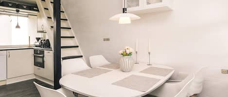Une cuisine moderne avec des meubles blancs, une cuisinière noire et une table à manger blanche, accompagnée de quatre chaises.