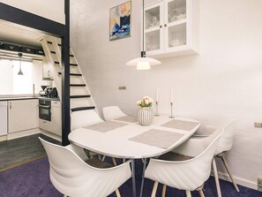 A modern kitchen with white cabinets, a black stove, and a white dining table with four chairs.