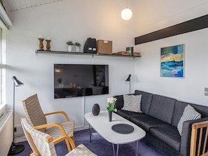 En moderne stue med sofa, stole, sofabord, fjernsyn og et billede på væggen.