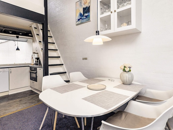 Et moderne køkken med spiseplads, med et hvidt bord med servietter, en vase med blomster og en trappe til en etage over.