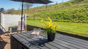 An outdoor seating area with a table, chairs, an umbrella, and a potted plant with yellow flowers. - 5 Person Holiday Home in Aabenraa (Aabenraa)