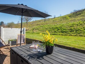 An outdoor seating area with a table, chairs, an umbrella, and a potted plant with yellow flowers. - 5 Person Holiday Home in Aabenraa (Aabenraa)