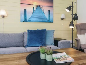 Un salon comprenant un canapé, une table basse avec un magazine, un tableau représentant une jetée et des lampes fixées au mur.