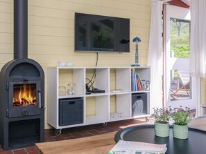 A living room with a wood-burning stove, a TV mounted on the wall, a white shelving unit, and a door leading outside. - 5 Person Holiday Home in Aabenraa (Aabenraa)