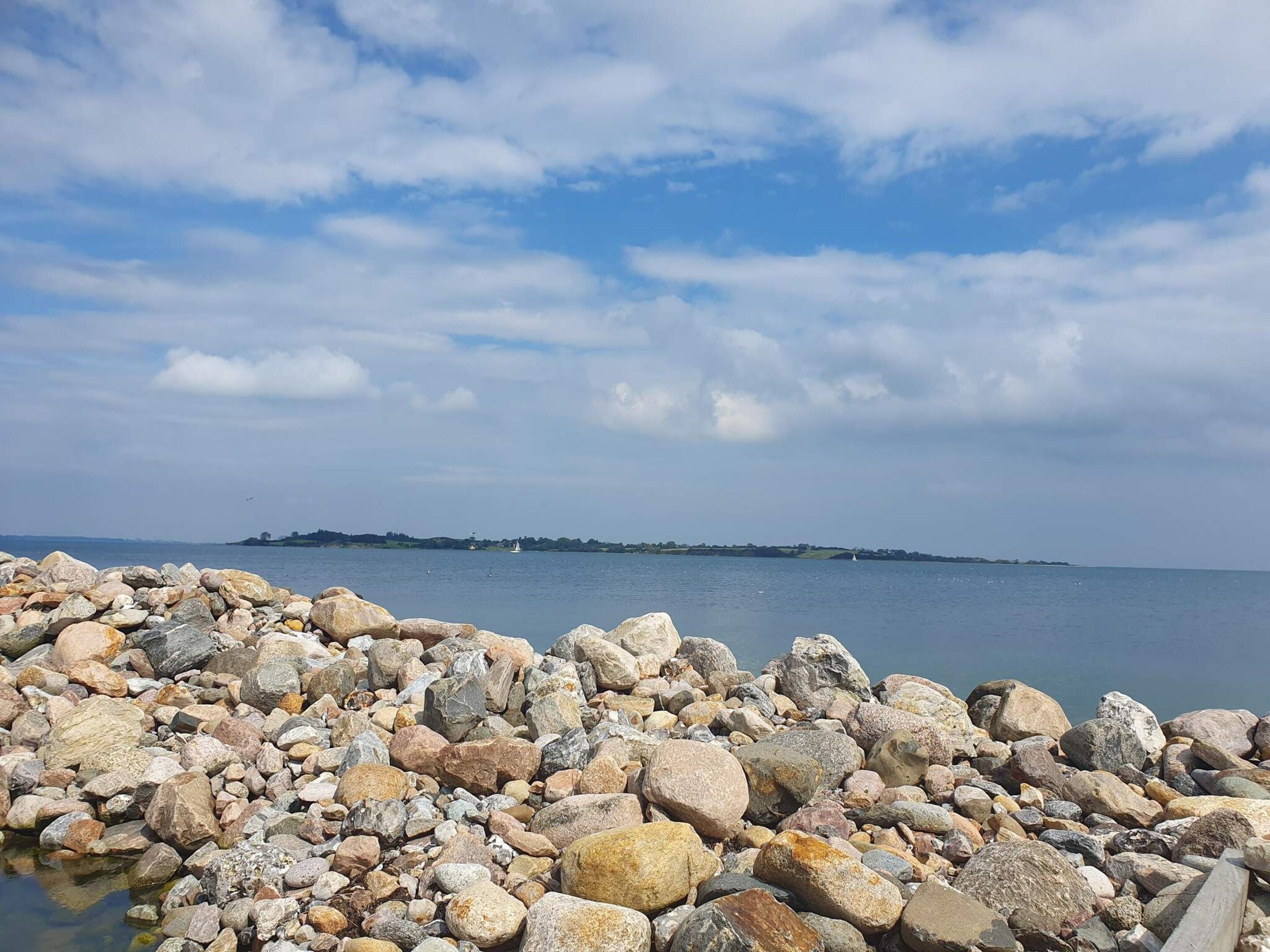 Una costa rocosa con un mar tranquilo y una tierra firme distante.