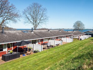 A row of cabins with a grassy slope in the foreground, a clear sky, and a body of water in the background. - 5 Person Holiday Home in Aabenraa (Aabenraa)