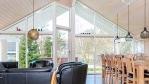 A spacious living area with a large window, a dining table with chairs, and a black leather sofa.