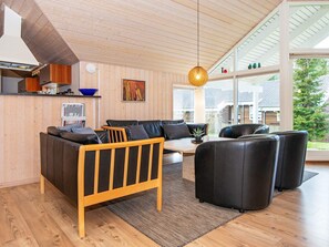 Un salon moderne avec un plafond en bois, un ensemble de canapés, une table basse et un luminaire suspendu.