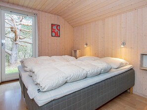 Une chambre avec un grand lit, des murs en bois, une fenêtre donnant sur les arbres et un luminaire fixé au mur.