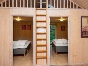 A wooden cabin with two beds, a ladder, and a view of greenery outside.