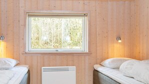 A room with two beds, a window with a view of trees, and a wall-mounted heater.