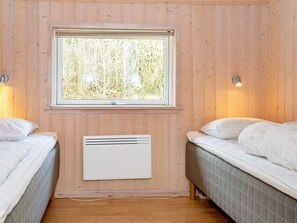 A room with two beds, a window with a view of trees, and a wall-mounted heater.